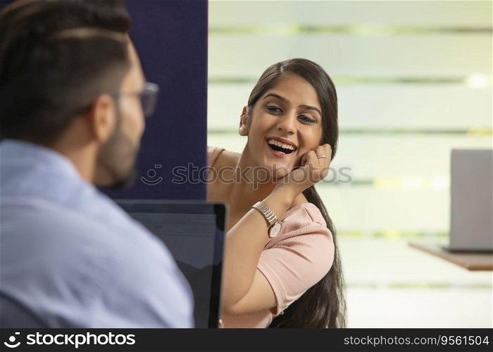 A HAPPY EXECUTIVE TALKING TO HER COLLEAGUE WHILE SITTING IN HER CUBICLE