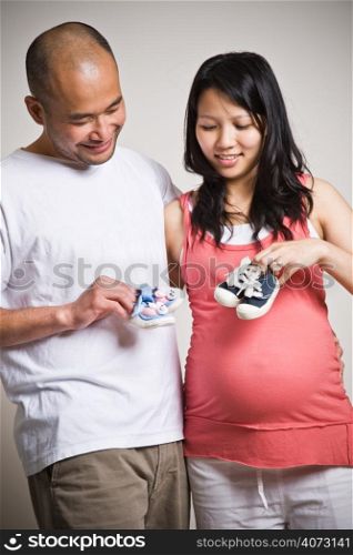 A happy expecting asian couple holding their unborn baby shoes