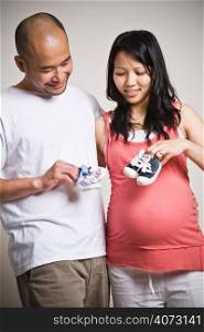 A happy expecting asian couple holding their unborn baby shoes