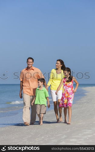 A happy family of mother, father and two children, son and daughter, walking holding hands and having fun in the sand of a deserted sunny beach