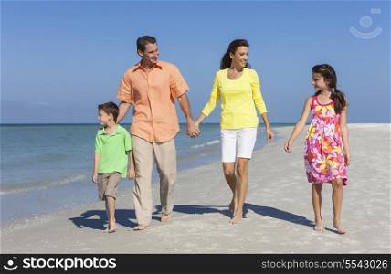 A happy family of mother, father and two children, son and daughter, walking holding hands and having fun in the sand of a deserted sunny beach