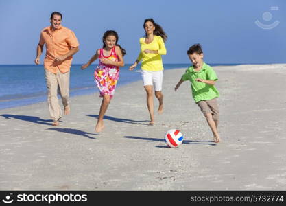 A happy family of mother, father and two children, son and daughter, running playing soccer or football in the sand of a sunny beach