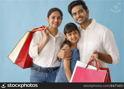 A HAPPY FAMILY POSING IN FRONT OF CAMERA WITH SHOPPING BAGS IN HAND