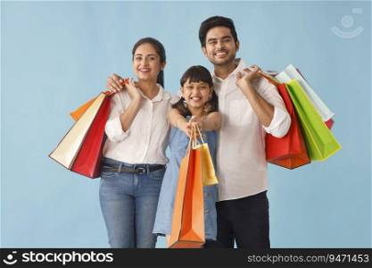 A HAPPY FATHER MOTHER AND DAUGHTER POSING WITH SHOPPING BAGS IN HAND
