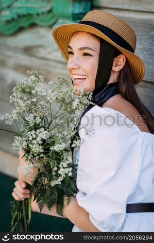 A happy girl in a small hat and with a bouquet of flowers.. A joyful portrait of a young girl with a bouquet of wildflowers and a hat 3