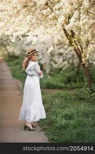 A happy girl walks in the alley of flowering trees.. A girl in a white dress walks near a cherry blossom 2706.