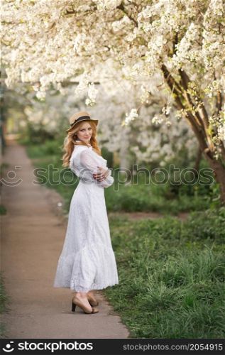 A happy girl walks in the alley of flowering trees.. A girl in a white dress walks near a cherry blossom 2707.