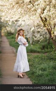 A happy girl walks in the alley of flowering trees.. A girl in a white dress walks near a cherry blossom 2707.