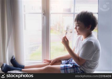 A Happy kid eating some ice cream, Portrait of a handsome young boy sitting next to a window having a refreshment, Child with a smiling face relaxing at home. Kid looking at camera