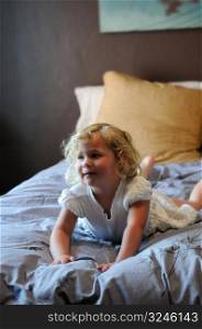 A happy little girl with blonde hair and a white dress plays on her parents bed