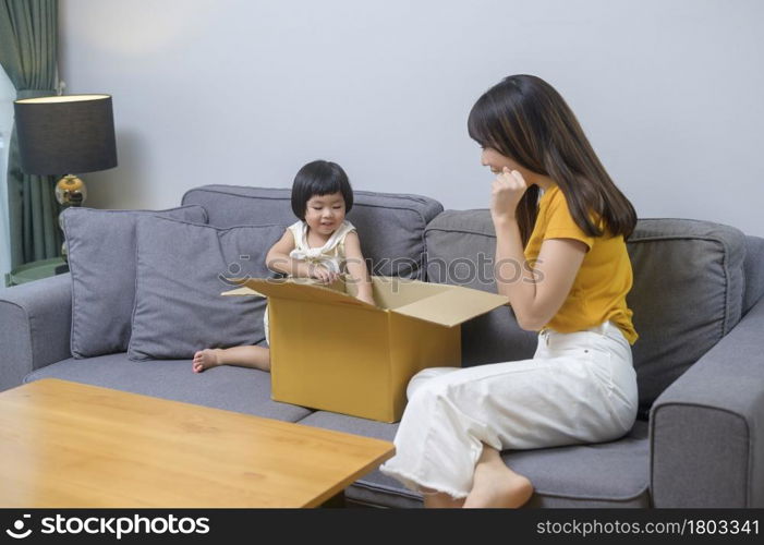 A happy mom with daughter opening cardboard box in living room at home. Happy mom with daughter opening cardboard box in living room at home