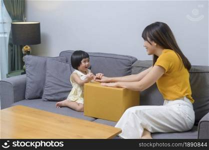 A happy mom with daughter opening cardboard box in living room at home. Happy mom with daughter opening cardboard box in living room at home
