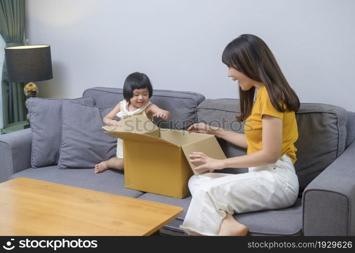 A happy mom with daughter opening cardboard box in living room at home. Happy mom with daughter opening cardboard box in living room at home