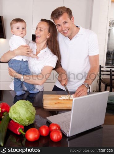 A happy mother and father with young toddler son, having fun making food in the kitchen with online recipe