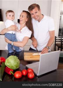 A happy mother and father with young toddler son, having fun making food in the kitchen with online recipe