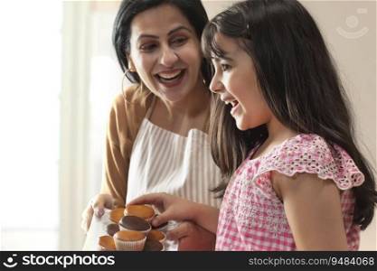 A HAPPY MOTHER GIVING CUPCAKES TO DAUGHTER