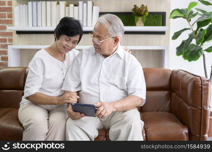 A happy senior Asian couple is using tablet and talking with family on webcam at home, retirement concept.