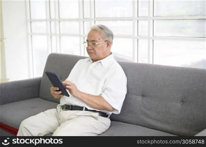 A happy senior Asian man is using tablet and talking with family on webcam at home, retirement concept.