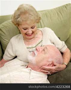 A happy senior couple relaxing together at home. Focus is on him looking up at her.