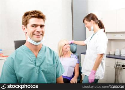 A happy smiling dentist at a clinic with an assistant and patient