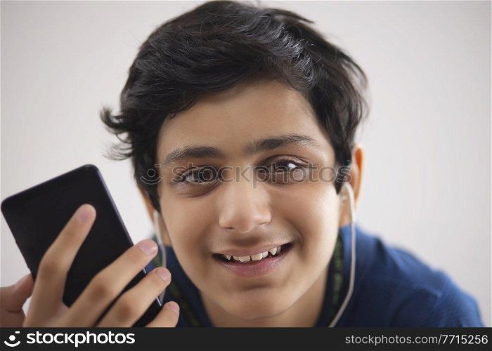 A HAPPY TEENAGE BOY LOOKING AT CAMERA WHILE HOLDING MOBILE PHONE