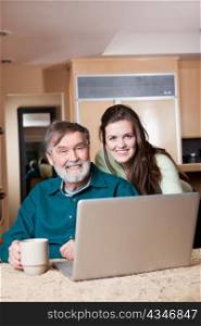 A happy teenage girl and her grandpa working on a laptop