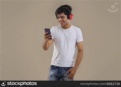 A HAPPY TEENAGER HOLDING MOBILE PHONE AND LISTENING TO MUSIC ON HEADPHONES