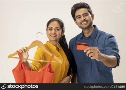 A HAPPY WOMAN SHOWS A NEWLY BOUGHT DRESS WHILE HUSBAND STANDS WITH DEBIT CARD