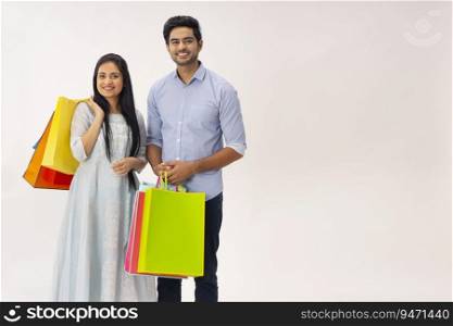 A HAPPY YOUNG COUPLE POSING IN FRONT OF CAMERA WITH SHOPPING BAGS IN HAND