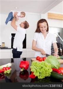 A happy young family in the kitchen, mother preparing food and father playing with son