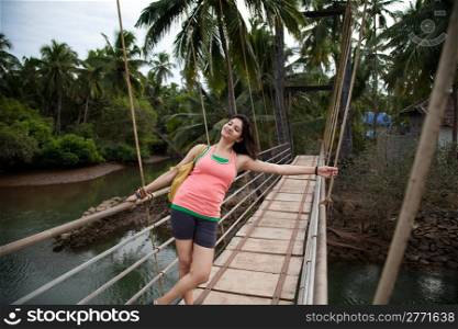 A happy young girl enjoying nature while relaxing on hanging bridge.