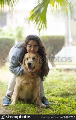 A HAPPY YOUNG GIRL IN A PARK HAPPILY CUDDLING PET DOG 