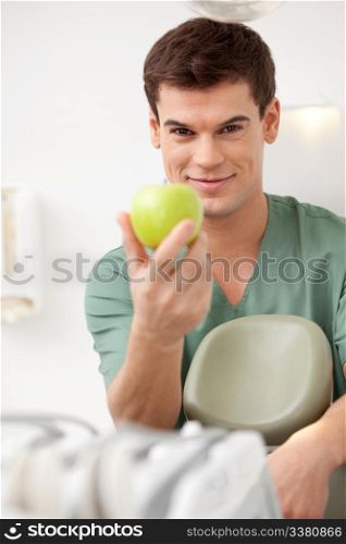A happy young male dentist holding an apple. Shallow depth of field, focus on dentist.
