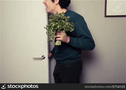 A happy young man holding a bunch of parsley is answering the door