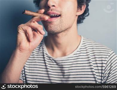 A happy young man in a stripey top is smoking a cigar
