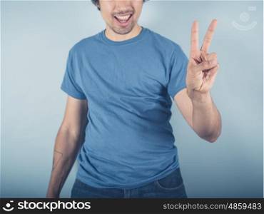 A happy young man in blue is displaying the V for victory sign