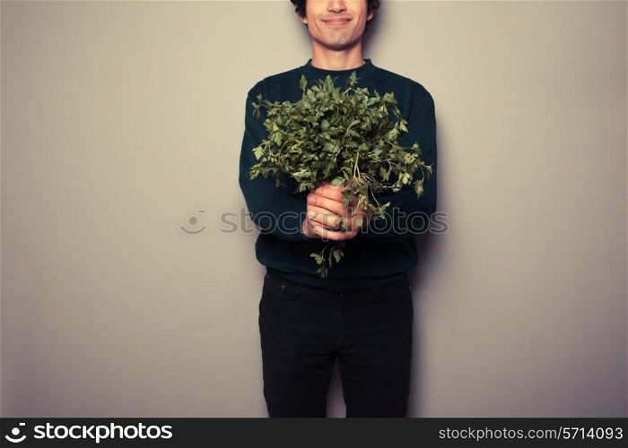 A happy young man is holding a big bunch of fresh parsley