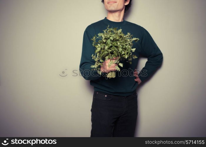 A happy young man is holding a big bunch of fresh parsley