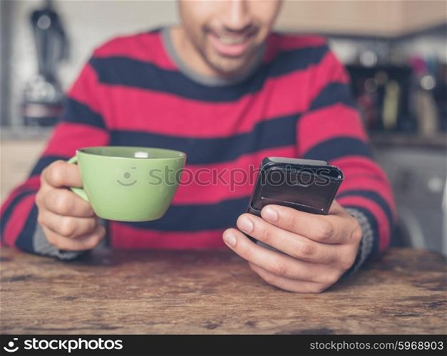 A happy young man is using a smart phone in a kitchen at home