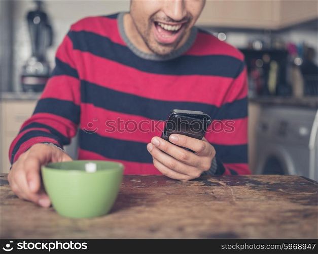 A happy young man is using a smart phone in a kitchen at home
