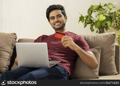 A HAPPY YOUNG MAN SITTING AT HOME AND DOING ONLINE TRANSACTIONS