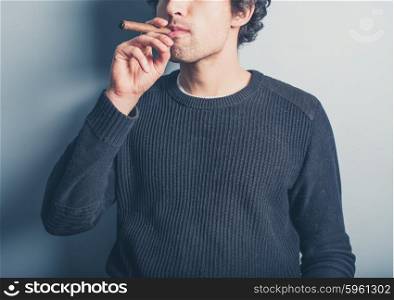 A happy young man wearing a black sweater is smoking a cigar