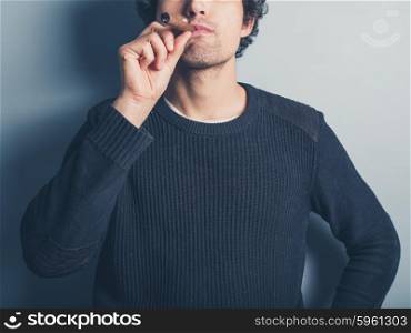 A happy young man wearing a black sweater is smoking a cigar