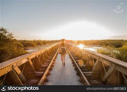 A happy young slender girl walks near a bridge in the rays of the summer sun. sunset on a summer day. A happy young slender girl walks near a bridge in the rays of the summer sun.