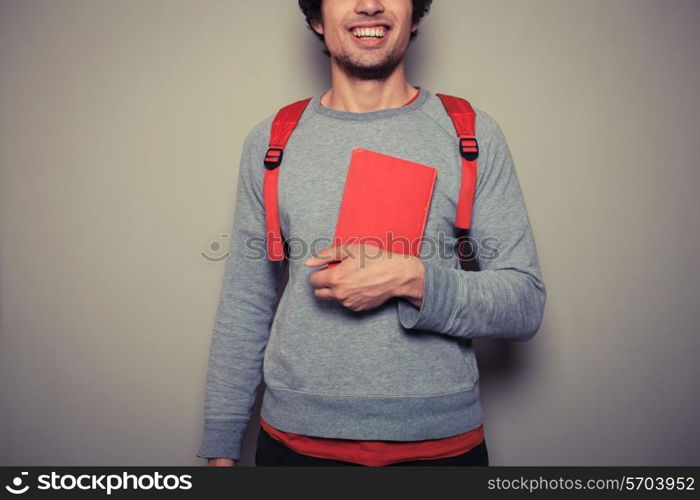 A happy young student wearing a red backpack is holding a red book