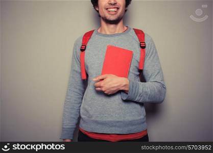 A happy young student wearing a red backpack is holding a red book