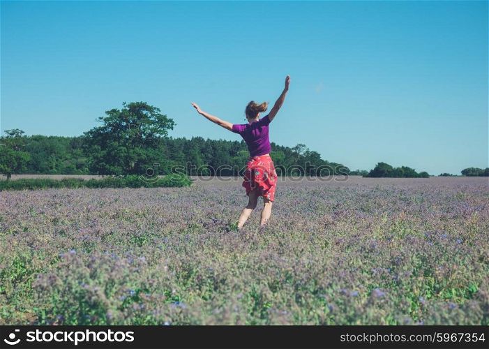 A happy young woman is jumping around in a field of purple flowers on a sunny summer day