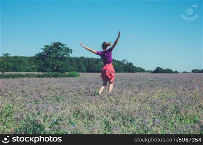A happy young woman is jumping around in a field of purple flowers on a sunny summer day