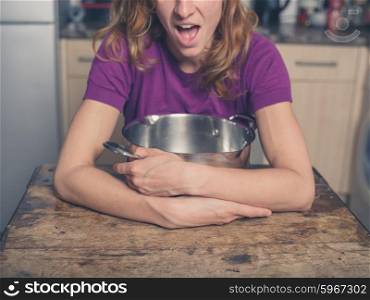 A happy young woman is sitting at a table in a kitchen with a pot