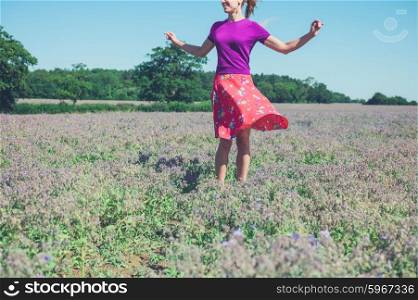 A happy young woman is spinning around in a field of purple flowers on a sunny summer day